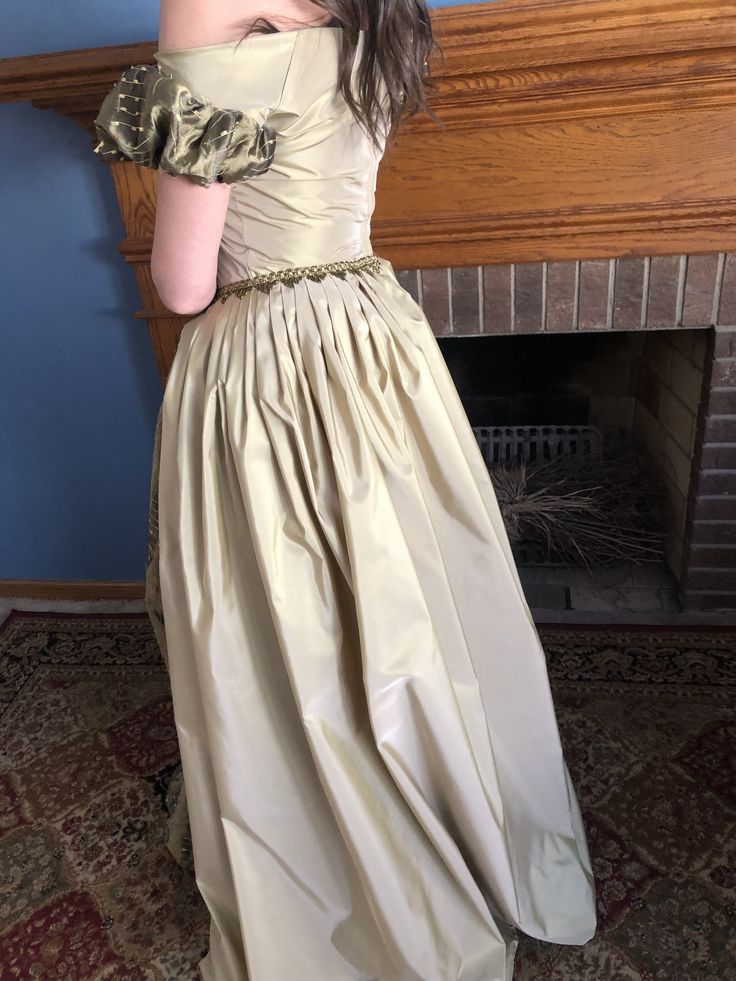 This is an elegant and beautiful gown that brings to mind Daphne from the Bridgertons. The gown is made of an exquisite raw silk and taffeta with a beautifully embellished golden trim. The over skirt is pleated around the waist for beautiful detailing to emphasize the silk contrast of the gown. This gown makes a lovely soft rustling sound as you move. It is an off the shoulder gown with puffed sleeves. The gown is fully lined with a zipper closure in the back. These are made to order and I would Taffeta Ball Gown With Sweep Train, Fitted Ball Gown With Pleated Back, Fitted Taffeta Ball Gown For Debutante Ball, Fitted Taffeta Evening Dress For Debutante Ball, Pleated Gown With Fitted Bodice And Floor-length, Pleated Gown With Fitted Bodice, Pleated Floor-length Gown With Fitted Bodice, Gold Silk Gown For Formal Occasions, Fitted Taffeta Gown For Formal Occasions