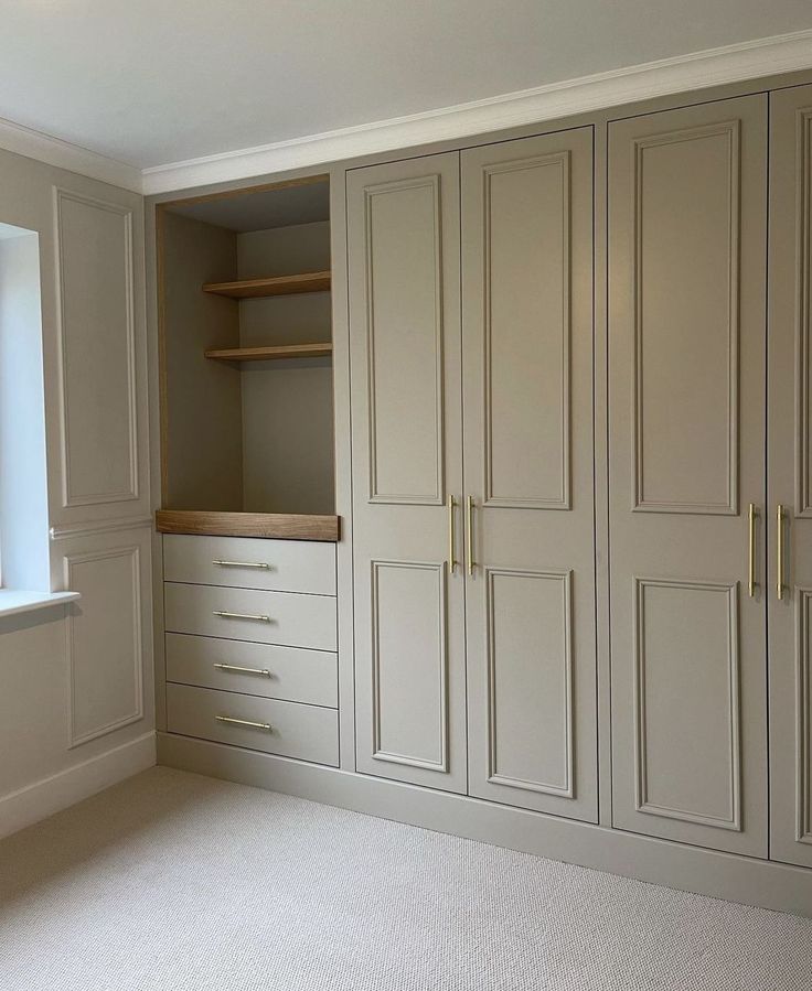 an empty room with white cupboards and shelves in the corner, next to a window