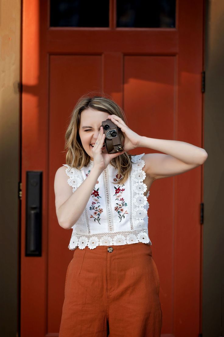 a woman holding a camera up to her face while standing in front of a red door