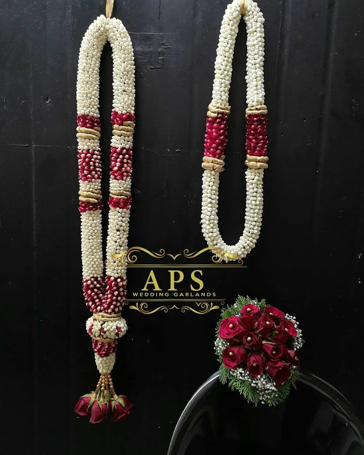 two white and red necklaces hanging from a black wall next to a vase with flowers