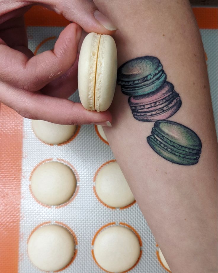 a person holding a macaroni and cheese tattoo on their arm, with other macaroons in the background