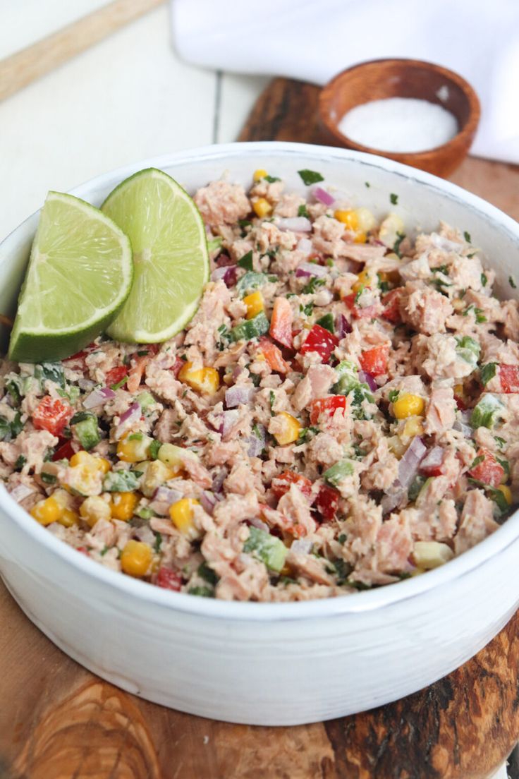 a white bowl filled with tuna salad on top of a wooden cutting board next to a lime wedge