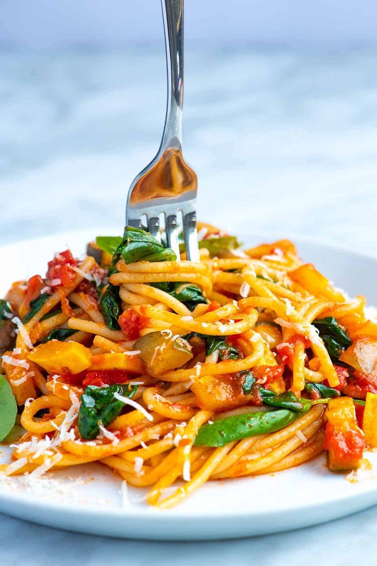 a white plate topped with pasta and spinach covered in tomato sauce next to a fork