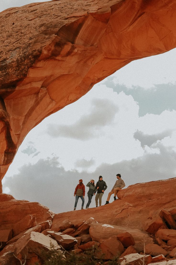 three people are standing under an arch in the desert, with rocks and boulders surrounding them