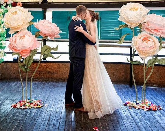 a bride and groom kissing in front of large paper flowers on the dancefloor