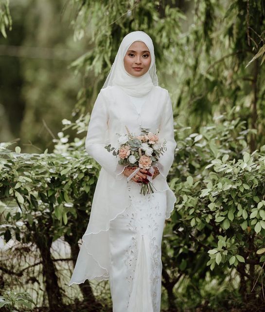 a woman wearing a white hijab and holding a bouquet