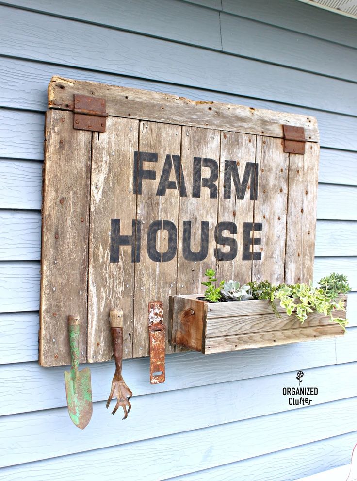 a wooden sign that says farm house hanging on the side of a blue building with gardening tools