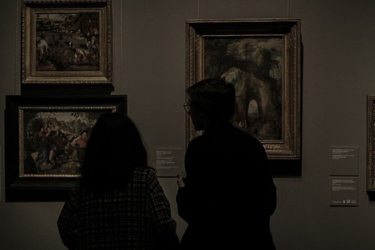 two people looking at paintings on display in a museum