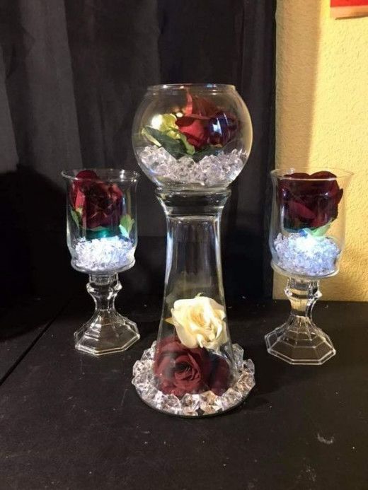 three glass vases with flowers in them on top of a black table next to a wall