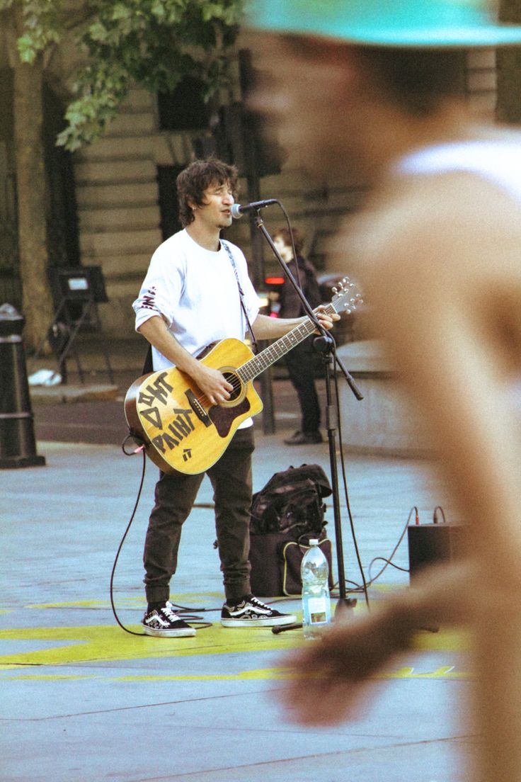 a shirtless man is playing guitar on the street while another person stands behind him