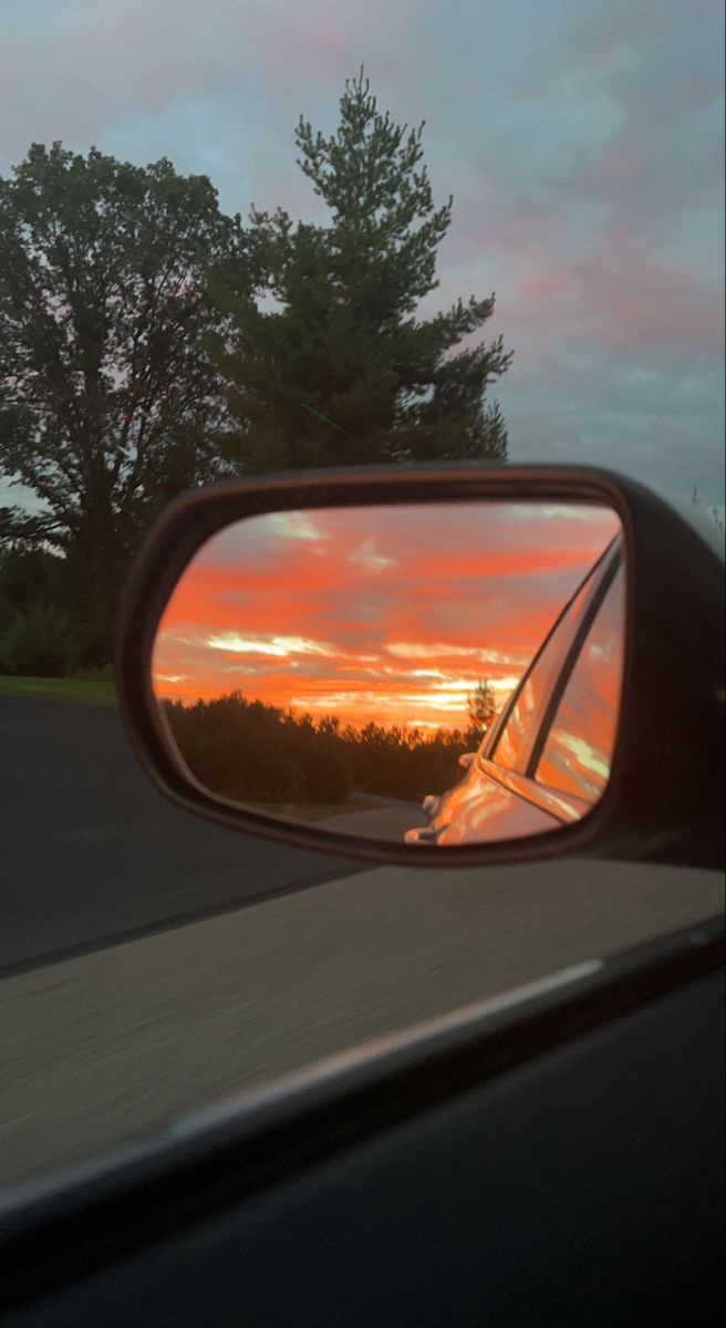 the sun is setting in the rear view mirror