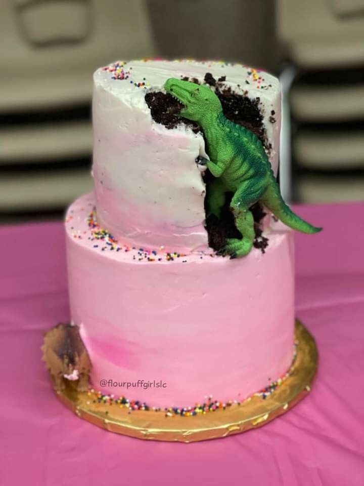 a pink and white cake with a green dinosaur on top