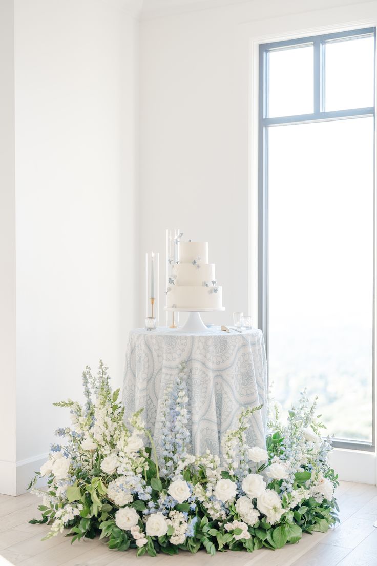 a wedding cake sitting on top of a table with white flowers and greenery around it