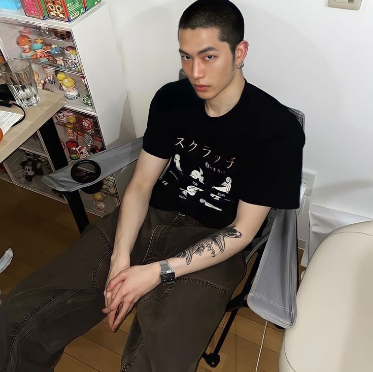 a young man sitting in a chair with tattoos on his arm and chest, looking at the camera