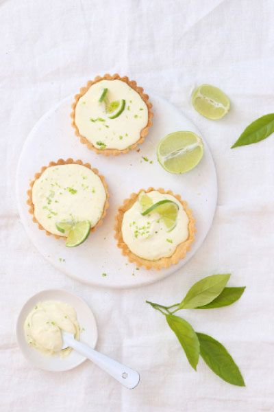 three small pies on a white plate with lime wedges next to them and two slices of lime