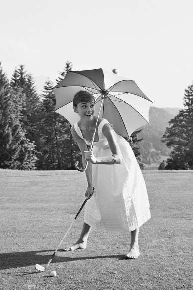 a woman holding an umbrella on top of a grass covered field with trees in the background