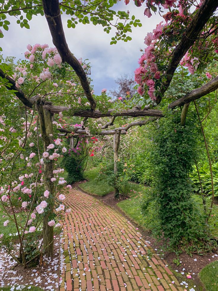 a brick path in the middle of a garden with pink flowers growing on it's sides