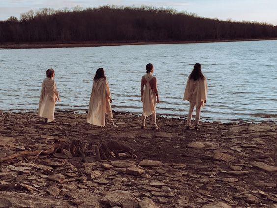 four women in white robes walking along the shore