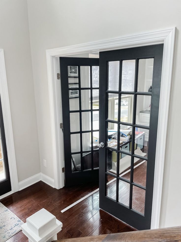 an open door leading to a living room with hardwood floors and white walls, in front of a large window