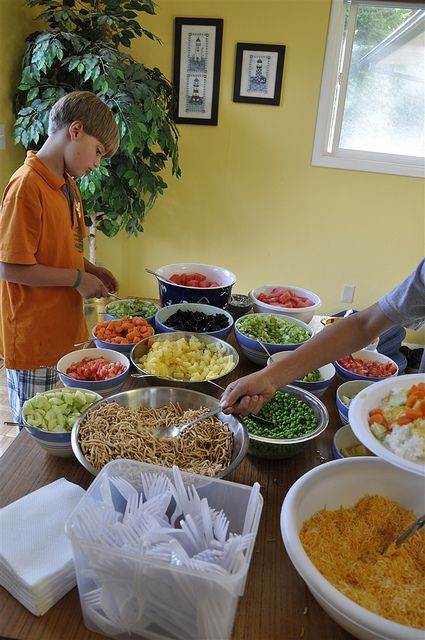 two people standing at a table filled with bowls of food and plates of salads