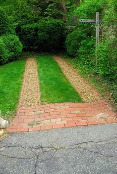 a brick path in the middle of a garden with green grass and bushes on either side