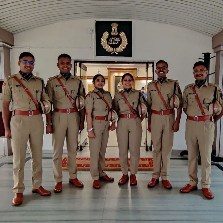 five uniformed men and women standing in front of an entrance to a building with flags on it