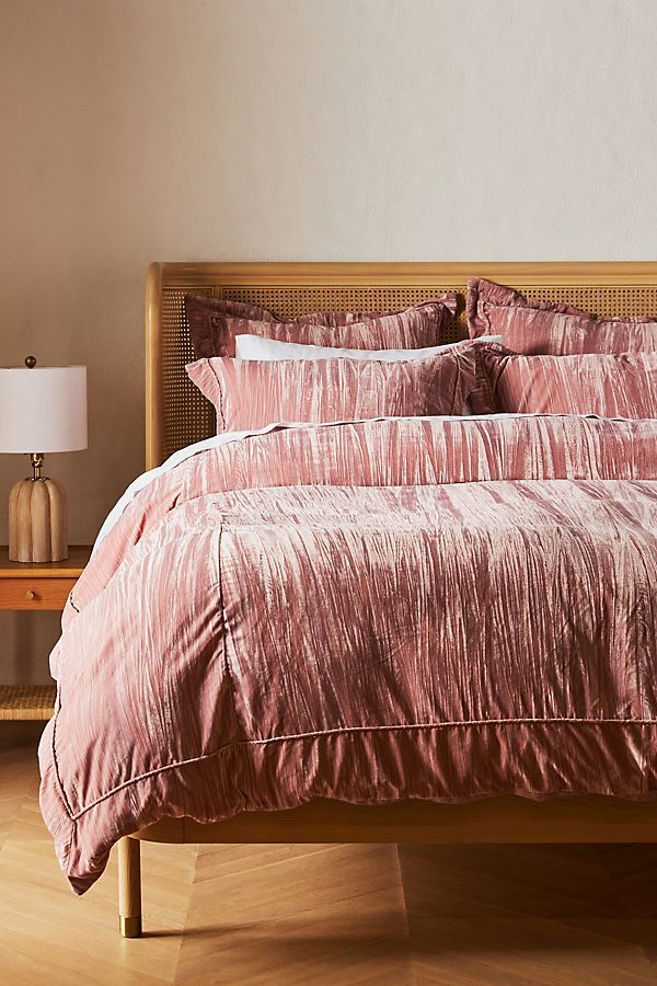 a bed with pink comforter and pillows in a white room next to a lamp