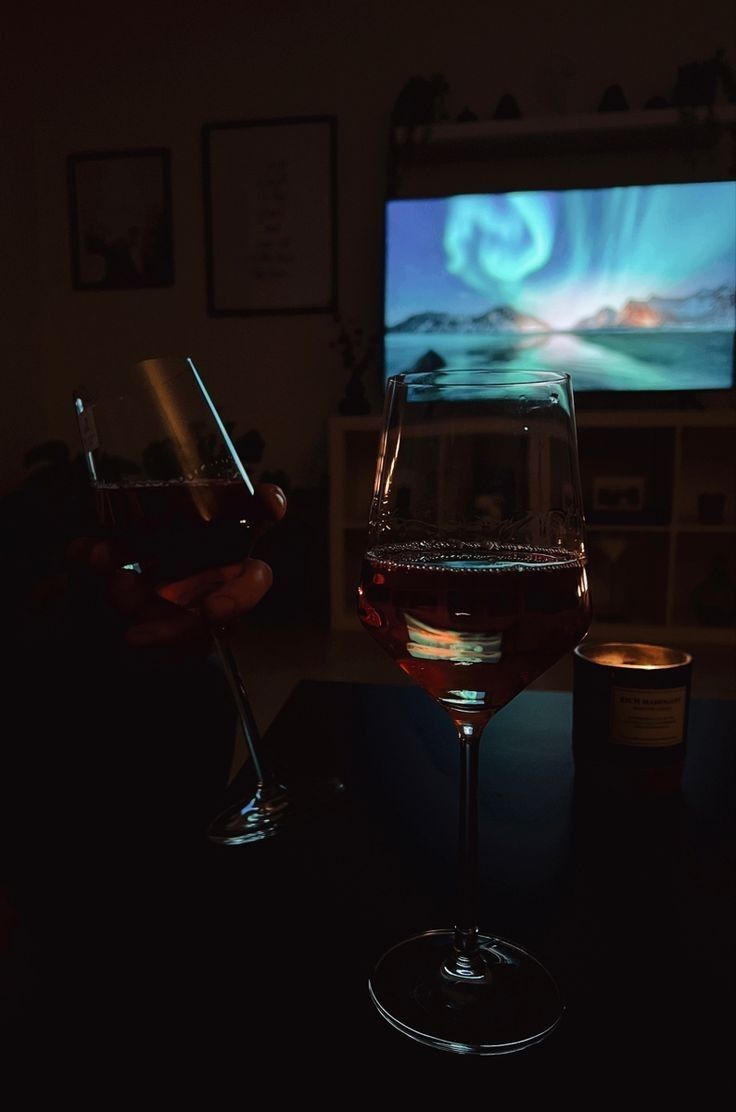 two glasses of wine sitting next to each other in front of a flat screen tv