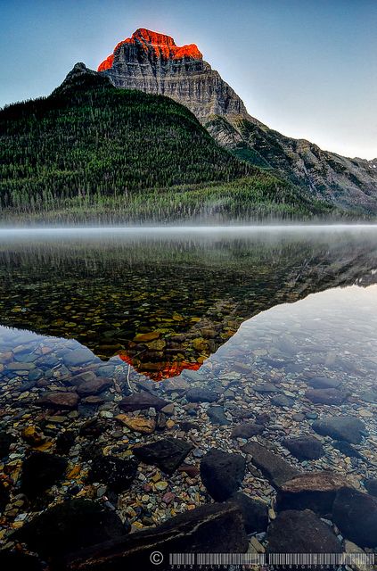 a mountain is reflected in the still water of a lake with rocks and trees around it