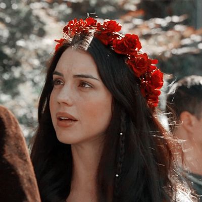 a woman with flowers in her hair standing next to other people and looking off into the distance