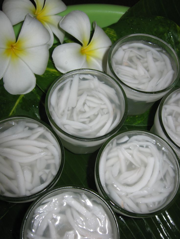 several small glass containers filled with white food on top of a green plate next to flowers