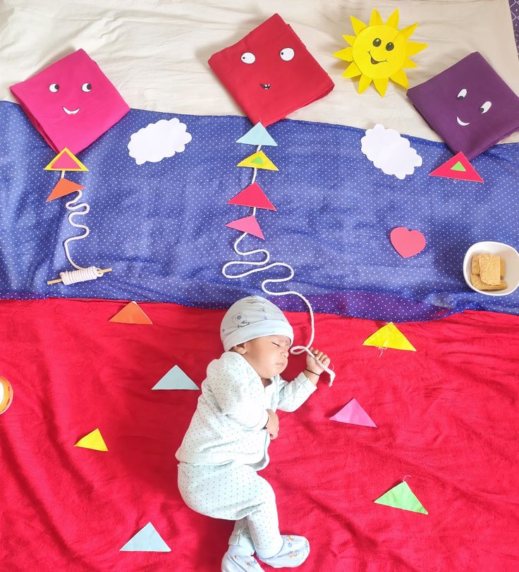 a baby is laying on a bed with colorful decorations and paper cutouts hanging from the ceiling