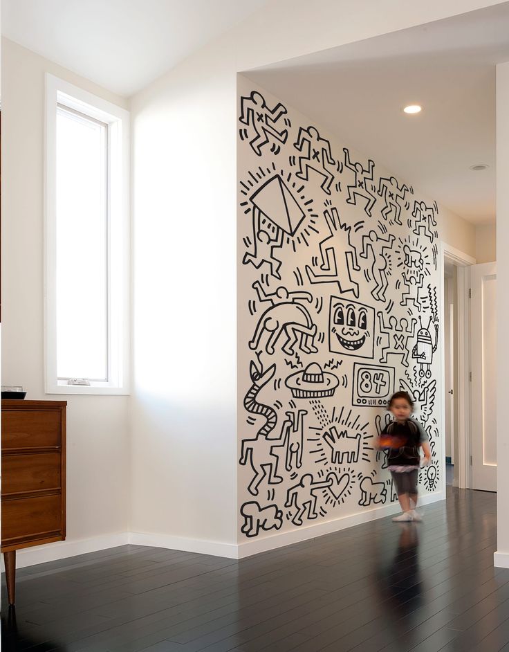 a little boy standing in front of a wall with black and white drawings on it