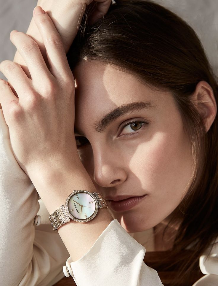 a woman in white shirt holding her hand near her face and looking at the camera