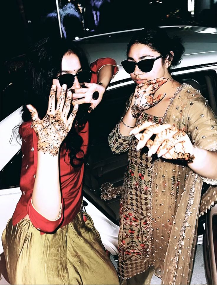 two women with their hands covered in hendi and makeup are standing next to a car