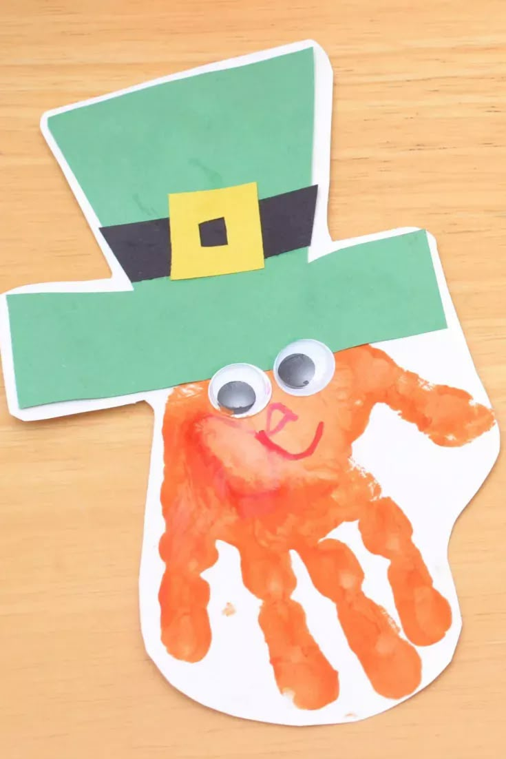 a paper plate with an orange handprint on it and a green hat over the top