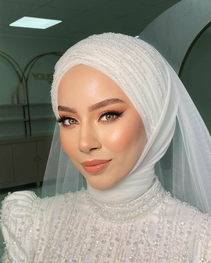 a woman wearing a white veil and dress with pearls on it's head is looking at the camera