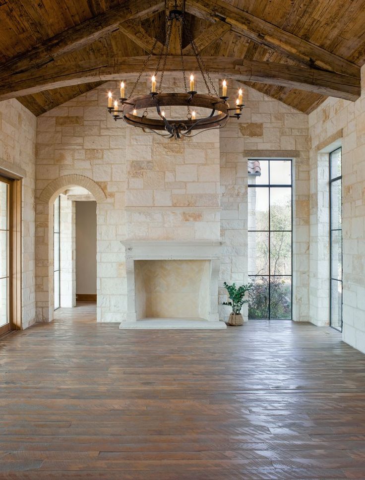 an empty room with wood floors and a chandelier hanging from the ceiling, surrounded by windows