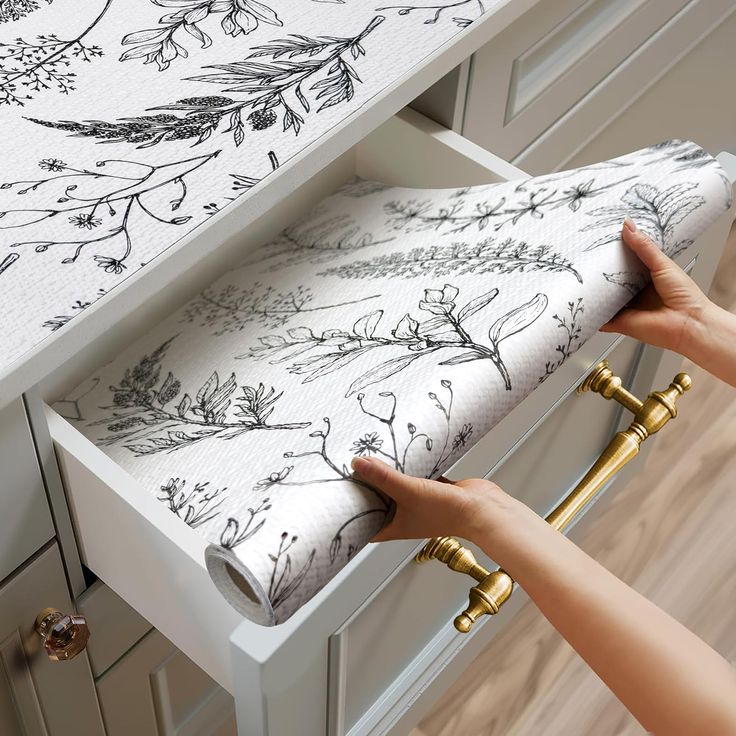 a woman is opening the drawers in her kitchen with floral wallpaper and gold handles