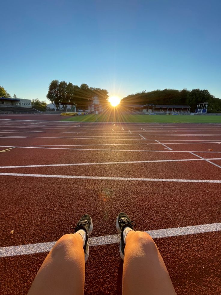 the sun is setting over a tennis court with someone's feet in the air