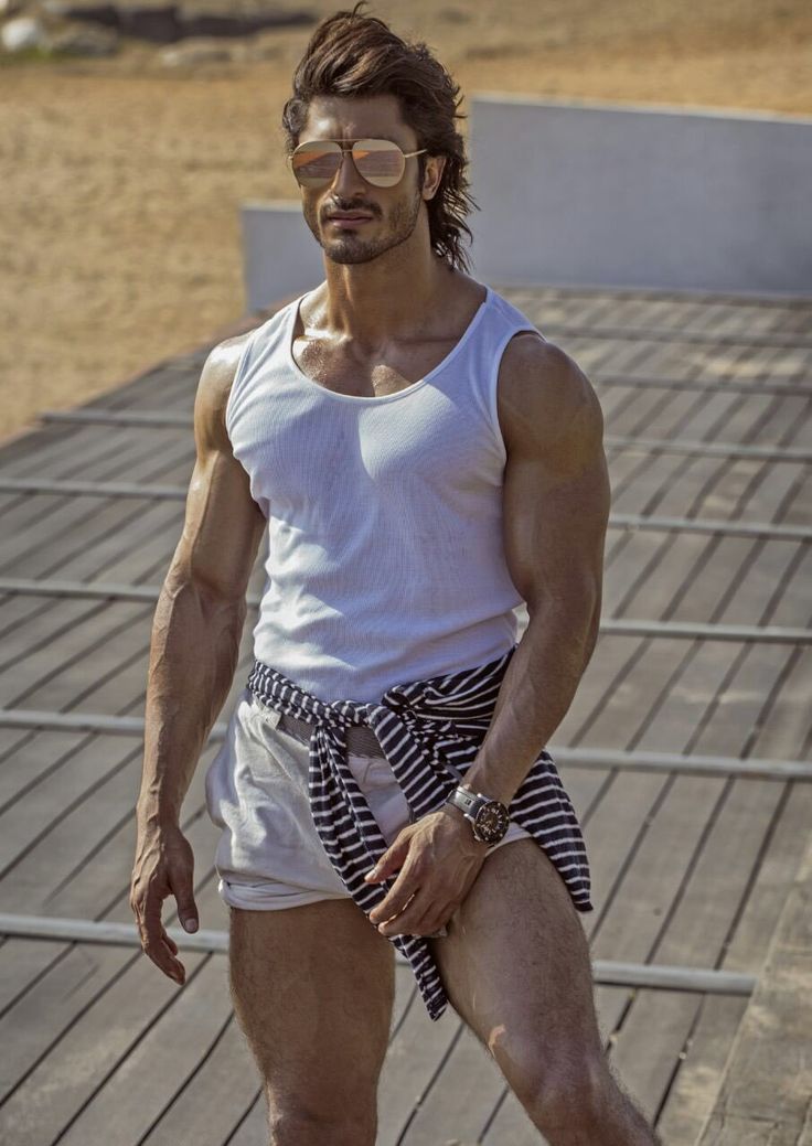 a man in white shirt and striped shorts standing on wooden floor next to metal railing