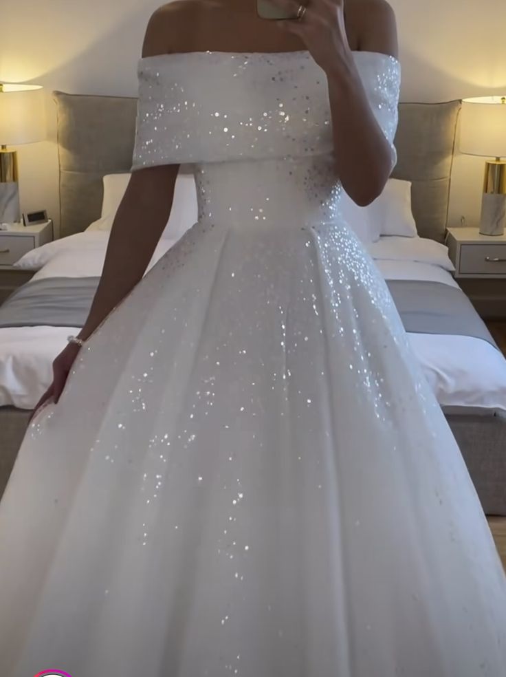 a woman in a white dress taking a selfie with her cell phone while standing next to a bed