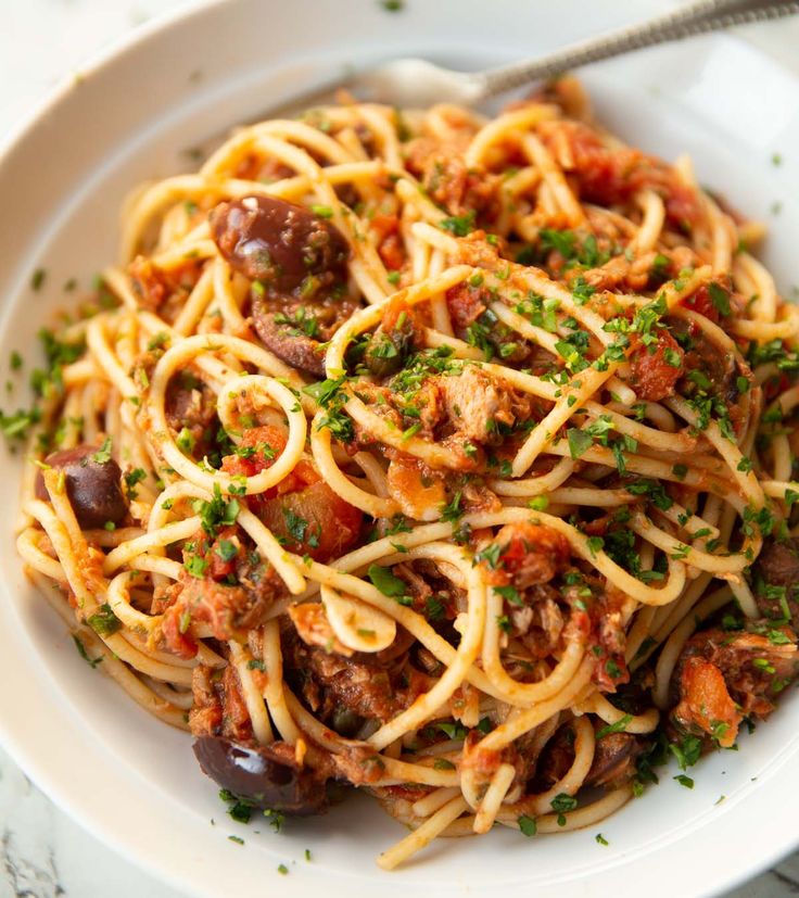 a white bowl filled with pasta and meat covered in sauce, parsley on the side