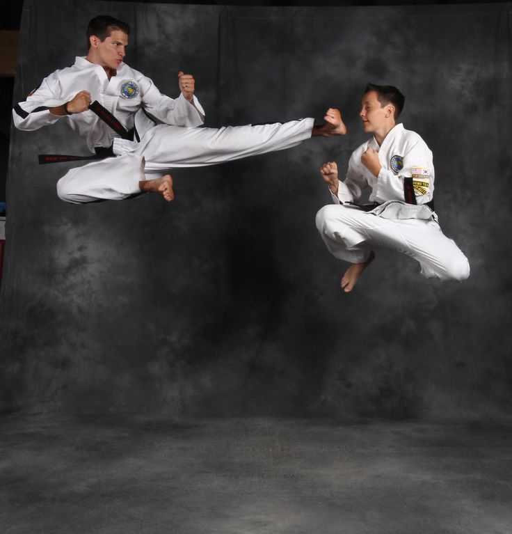 two men in white karate uniforms are doing tricks with their hands up and feet apart