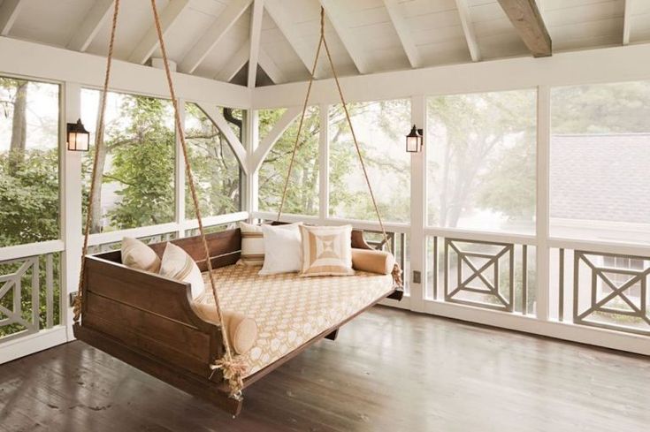 a porch swing with pillows on it in the middle of a room filled with windows