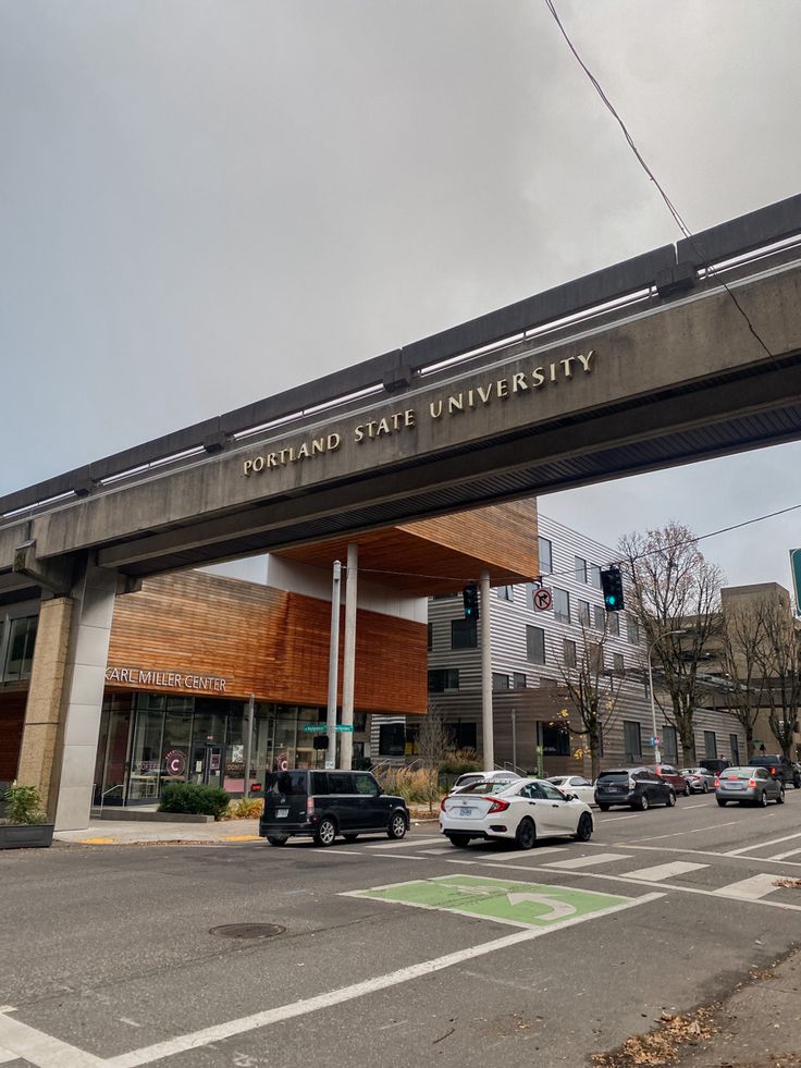 cars are driving under an overpass in front of a building with a sign that reads portland state university