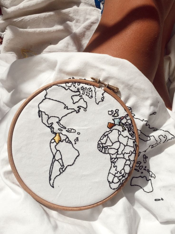 a person is holding a cross - stitch world map in their hand while laying on the bed