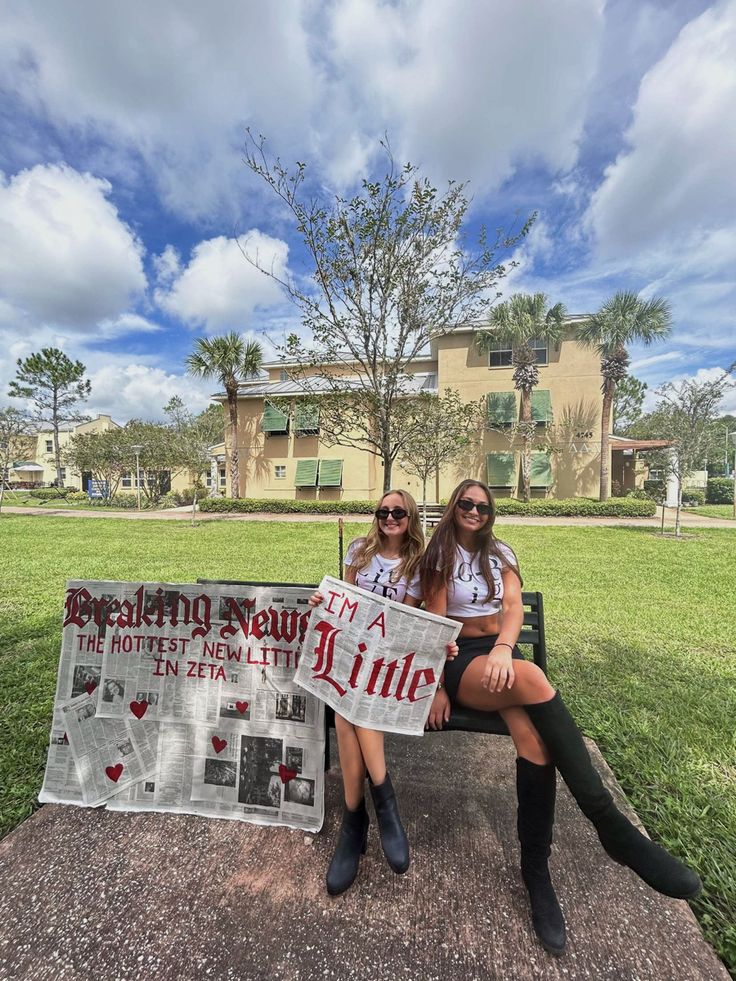 two women sitting on a bench holding a sign