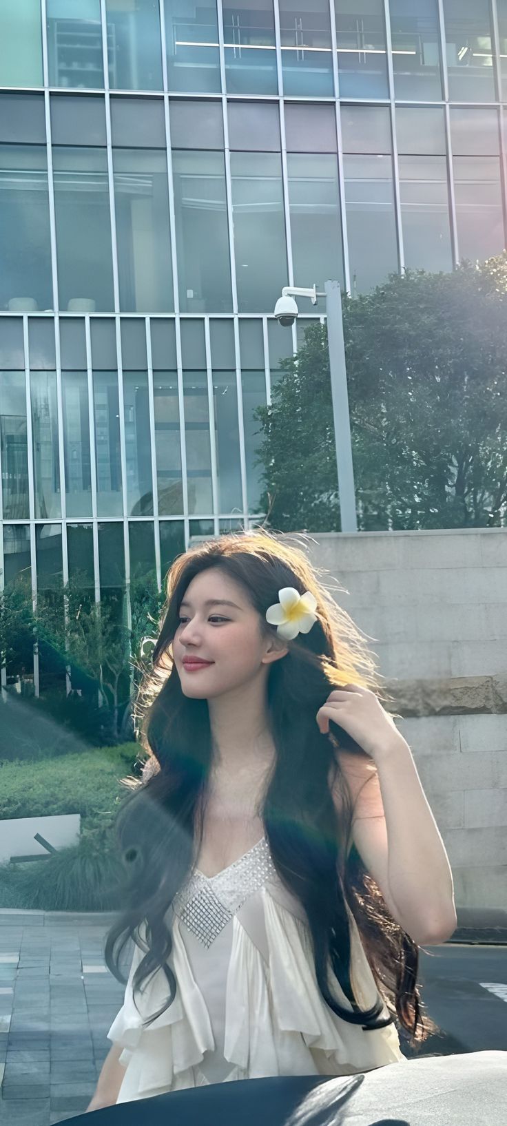 a woman with long black hair and a flower in her hair sitting on the hood of a car