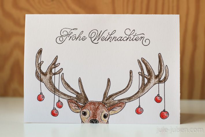 a christmas card with a deer's head and ornaments hanging from the antlers